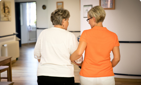 Eine Pflegerin bei Ihrer Ehrenamtlichen Tätigkeit Eine Seniorin wird von einer Pflegefachkraft über einen Flur geführt
